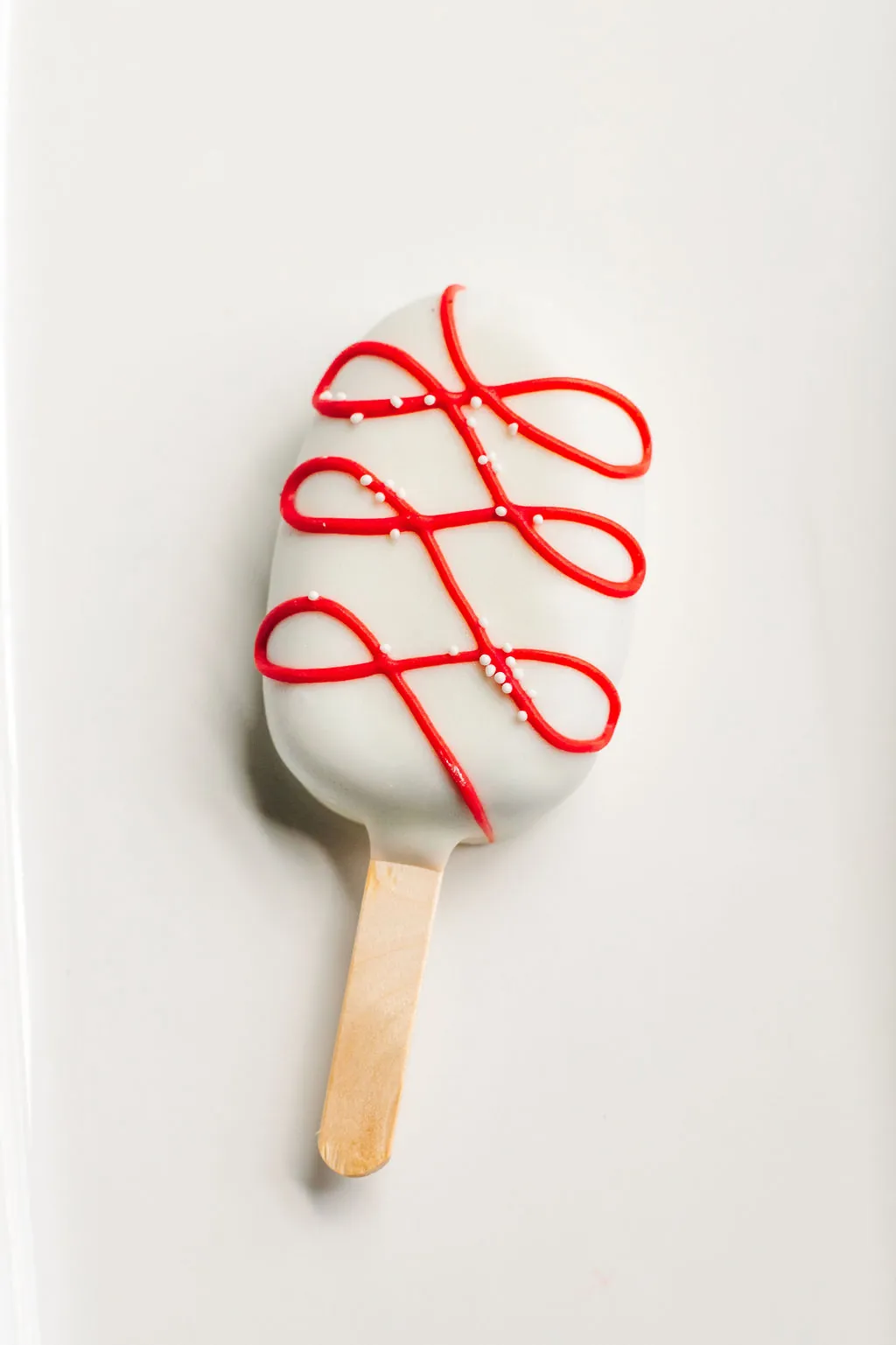 Close-up of a white cakesicle with looping red drizzle and small white nonpareils.